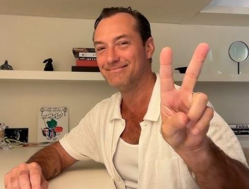 Jude Law w dynamicznej scenie, z intensywnym wyrazem twarzy, z rozmytym, filmowym tłem, symbolizującym jego wszechstronną karierę aktorską.