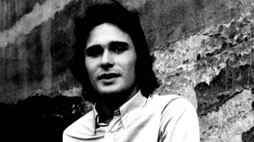 Jerzy Grunwald na scenie z zespołem En Face, z gitarą, w estetyce folk rocka lat 70., oddający energię i pasję muzycznego występu.