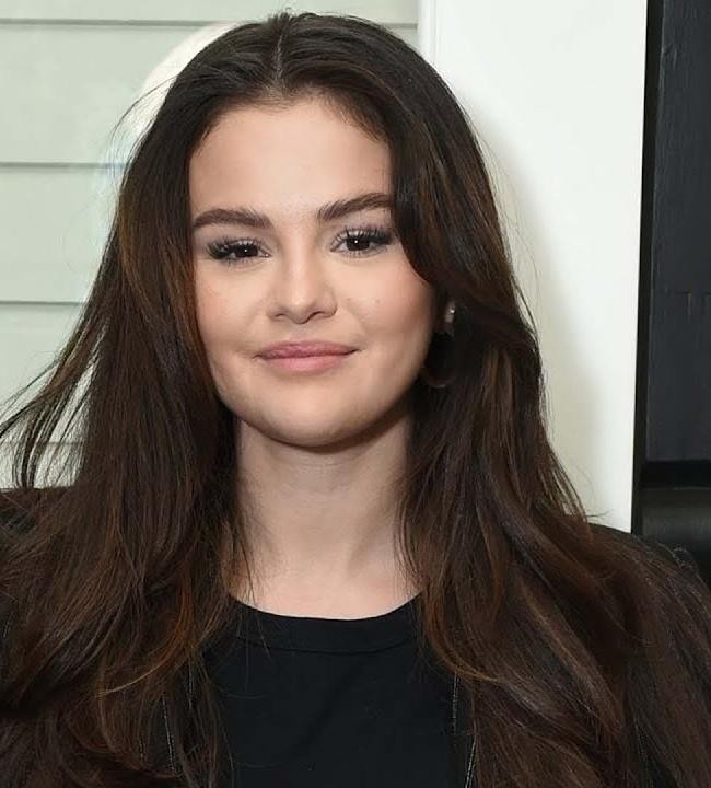 Selena Gomez na scenie podczas występu muzycznego, z mikrofonem w ręku i rozświetloną publicznością w tle.